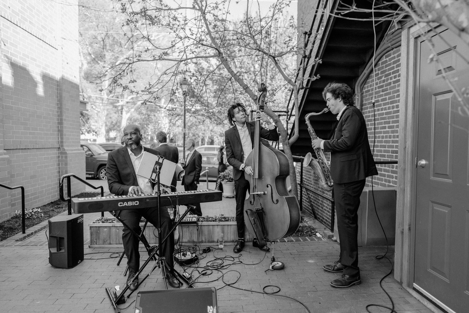 Keys, upright bass and saxophone playing a courtyard reception