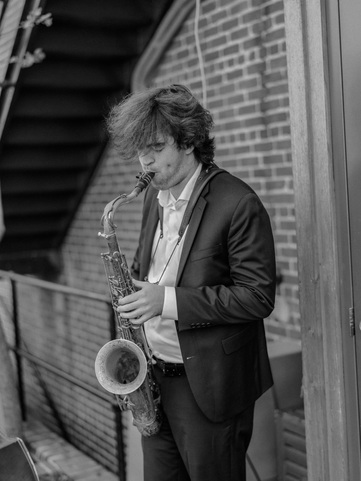 Saxophonist playing beside a brick wall